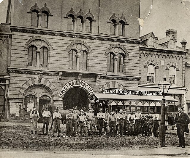A group in front of a horse-drawn streetcar in front of Yorkville Town Hall 1870. A gas streetlamp is visible in the right foreground.