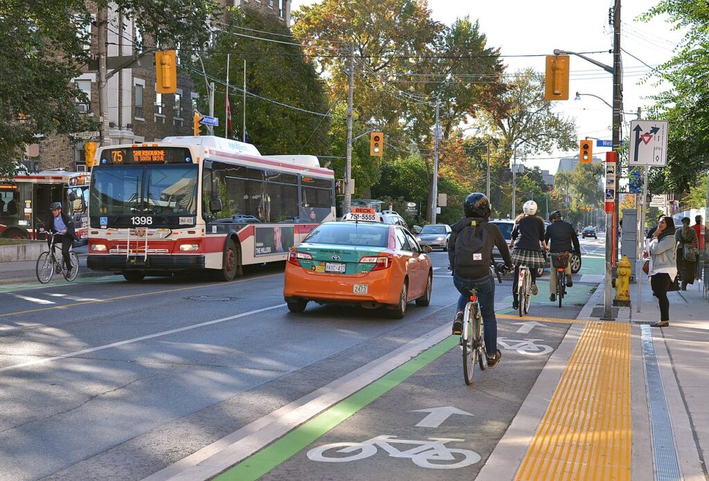 A roadway with bike lanes. A public bus service operated by the Toronto Transit Commission is visible in the background.